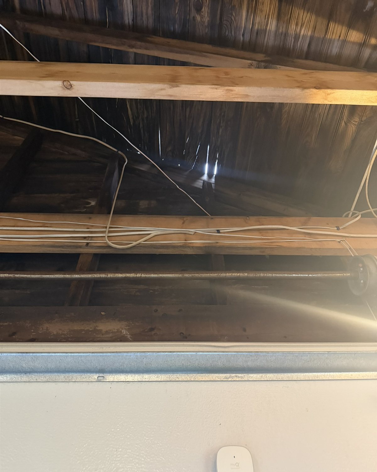 Interior attic view showing wooden beams and daylight visible through an exterior gap.