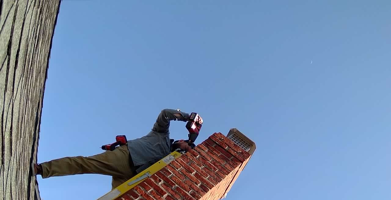 Wildwise technician on an extension ladder installing the chimney cap, viewed from below.